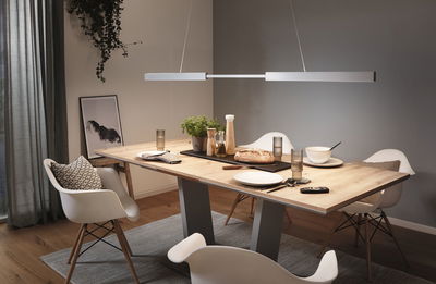 Modern light wood dining table with white chairs and minimalist pendant light in dining room setting.