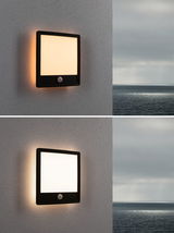 Black square outdoor wall light with motion sensor and warm white illumination on grey wall.