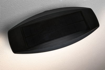 Schwarze Solarlampe mit rechteckigem Solarpanel und indirektem Licht an weißer Wand