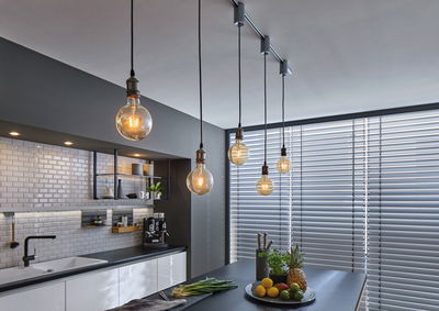 Cuisine moderne avec plans de travail noirs, carreaux blancs et cinq ampoules suspendues pour l'éclairage