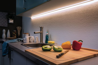 Plan de travail de cuisine moderne avec évier en acier inoxydable, lumière LED sous meuble et poivrons colorés sur planche en bois