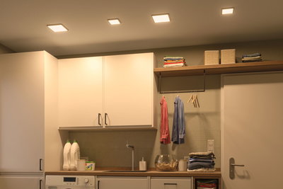 Moderne witte keukenkasten met houten werkblad en warmwitte LED-plafondlampen voor woonverlichting.