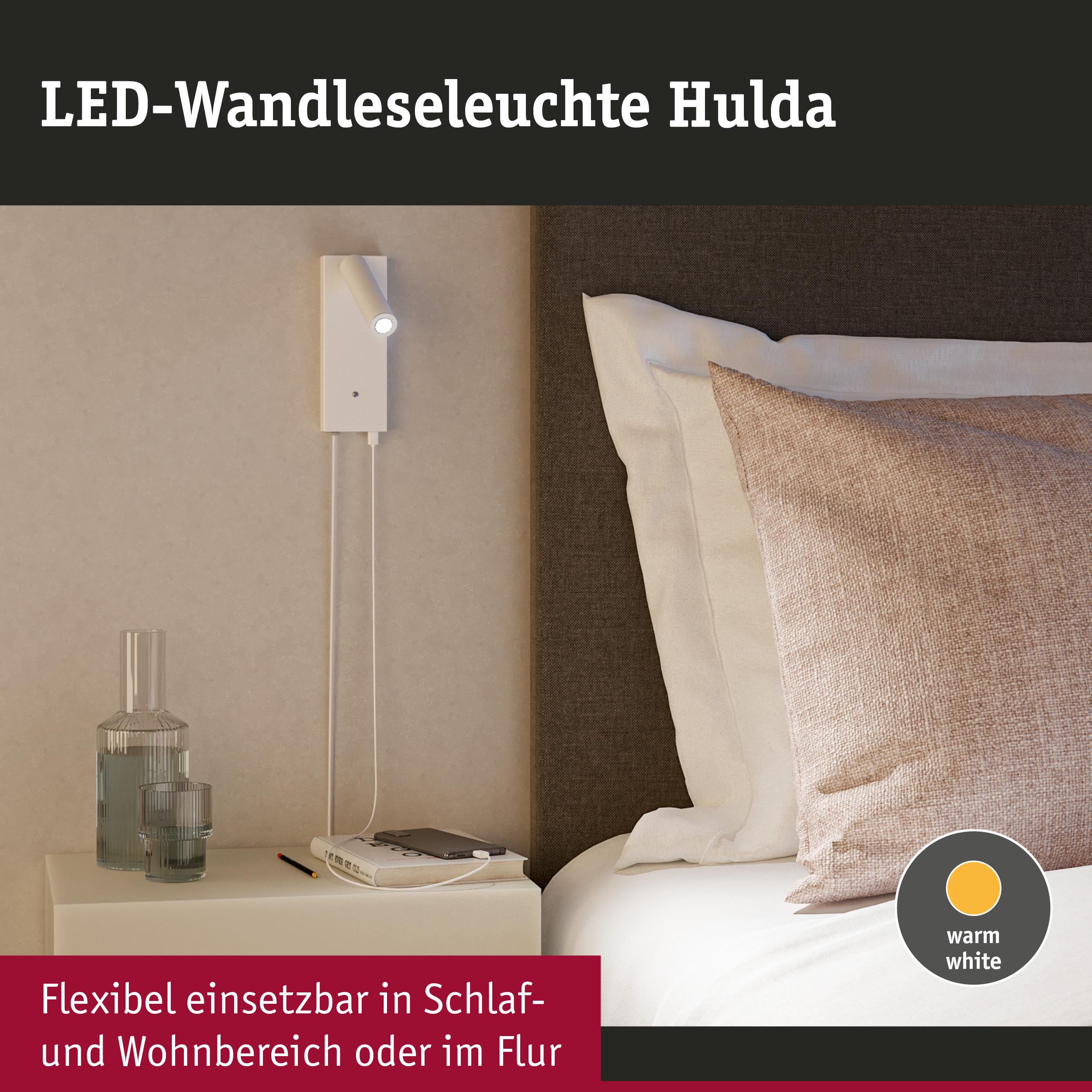 Weiße LED-Wandleseleuchte Hulda mit warmweißem Licht neben Bett und Nachttisch für Schlafzimmer.