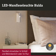 Weiße LED-Wandleseleuchte Hulda mit flexiblem Leuchtkopf und warmweißem Licht neben Bett und Nachttisch