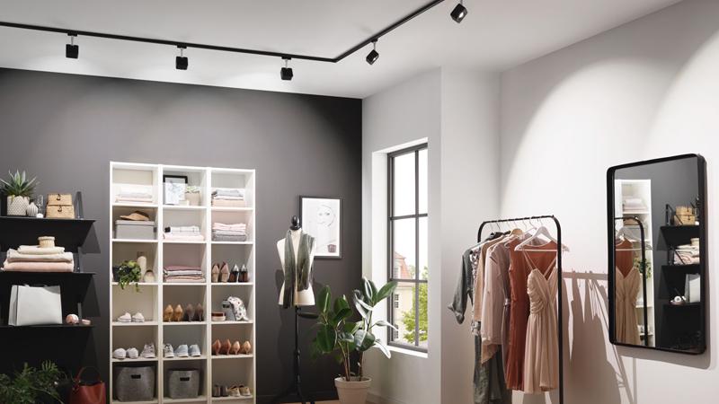 Modernes Ankleidezimmer mit schwarzer Schiene und LED-Strahlern, Kleiderständer und Spiegel an weißer Wand.