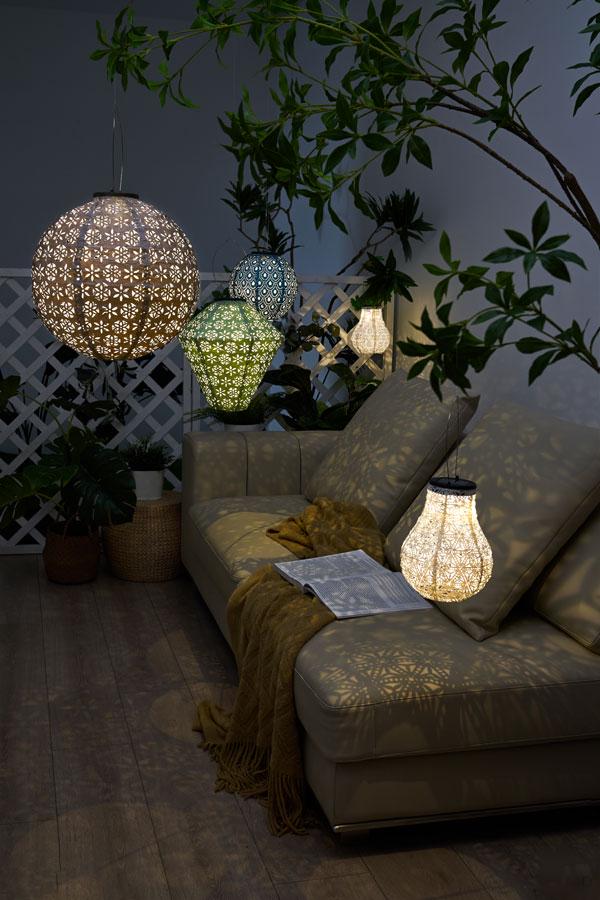 Mehrfarbige dekorative Hängelampen mit filigranen Mustern beleuchten gemütliche Sofaecke mit Pflanzen.