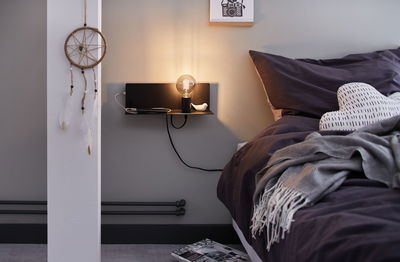 Schwarze Wandlampe mit Glühbirne und Ablage neben Bett mit dunkler Bettwäsche und Herz-Kissen
