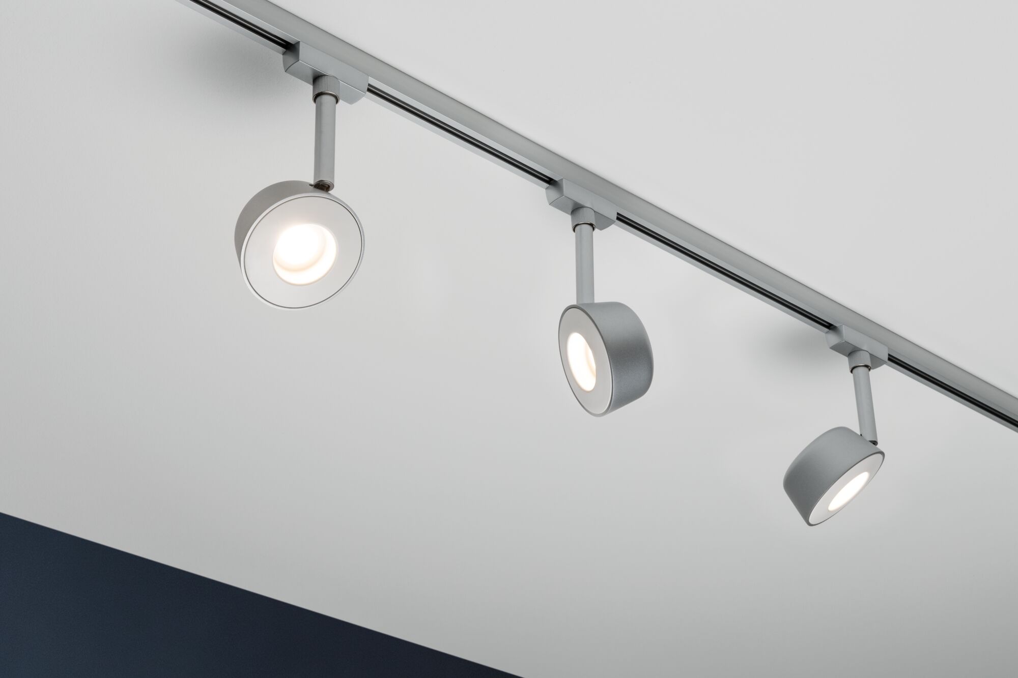 Tre sølvfarvede LED-skinnespotlights i metal monteret på hvidt loft til moderne indendørs belysning.