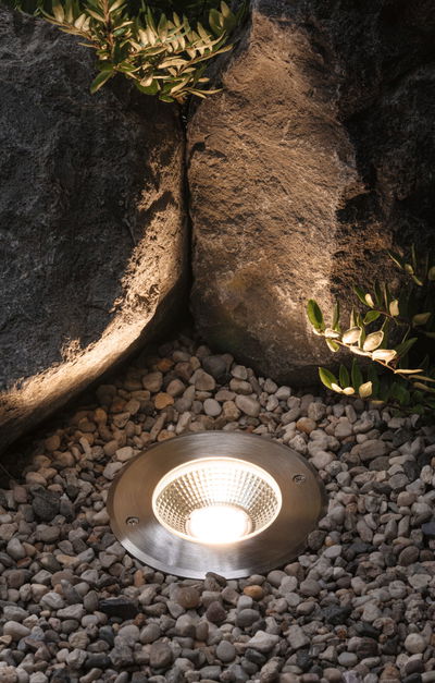 Recessed LED garden light in brushed stainless steel surrounded by pebbles for outdoor lighting