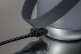 Nahaufnahme eines schwarzen Steckers an grauem Gerät mit schwarzem Gummiband auf reflektierender Oberfläche