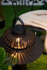 Zwarte metalen solar-lantaarn met handvat op tafel, warm licht voor tuin en terras