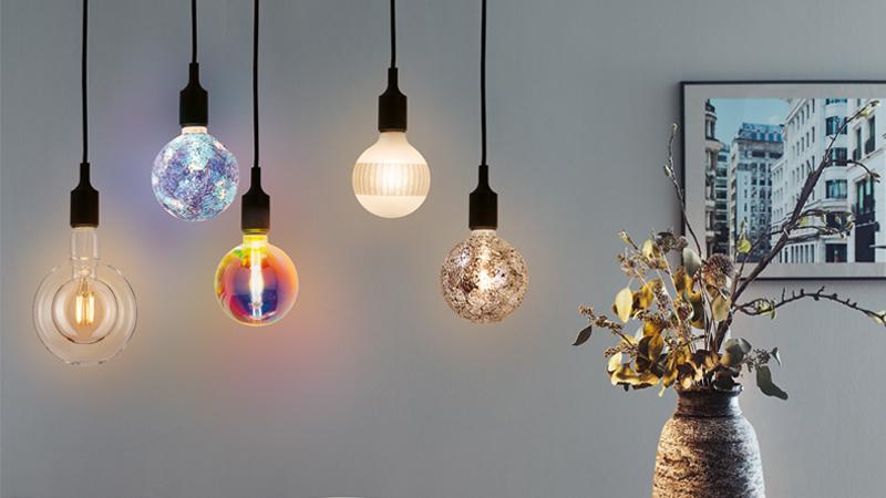 Cinq ampoules LED décoratives colorées suspendues dans une pièce moderne avec vase et photo urbaine.