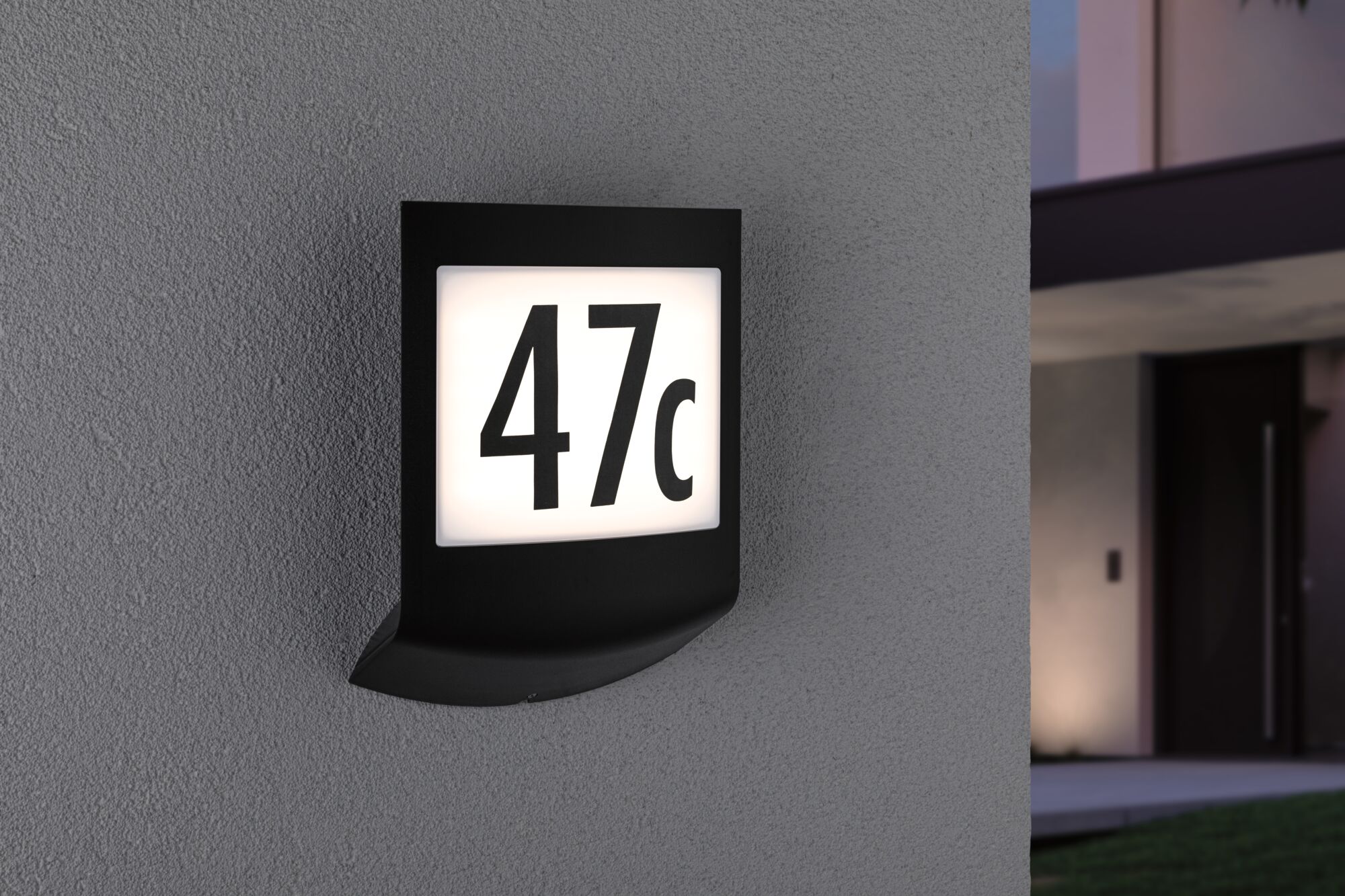 Schwarze LED-Hausnummernleuchte mit weißem beleuchtetem Feld und schwarzer Zahl 47c an grauer Wand