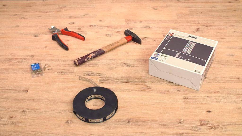 Tools and mounting materials on wooden table with hammer, pliers, nails, and metal strip for LED lighting