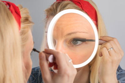 Woman applying black mascara using illuminated LED ring cosmetic mirror for precise makeup.