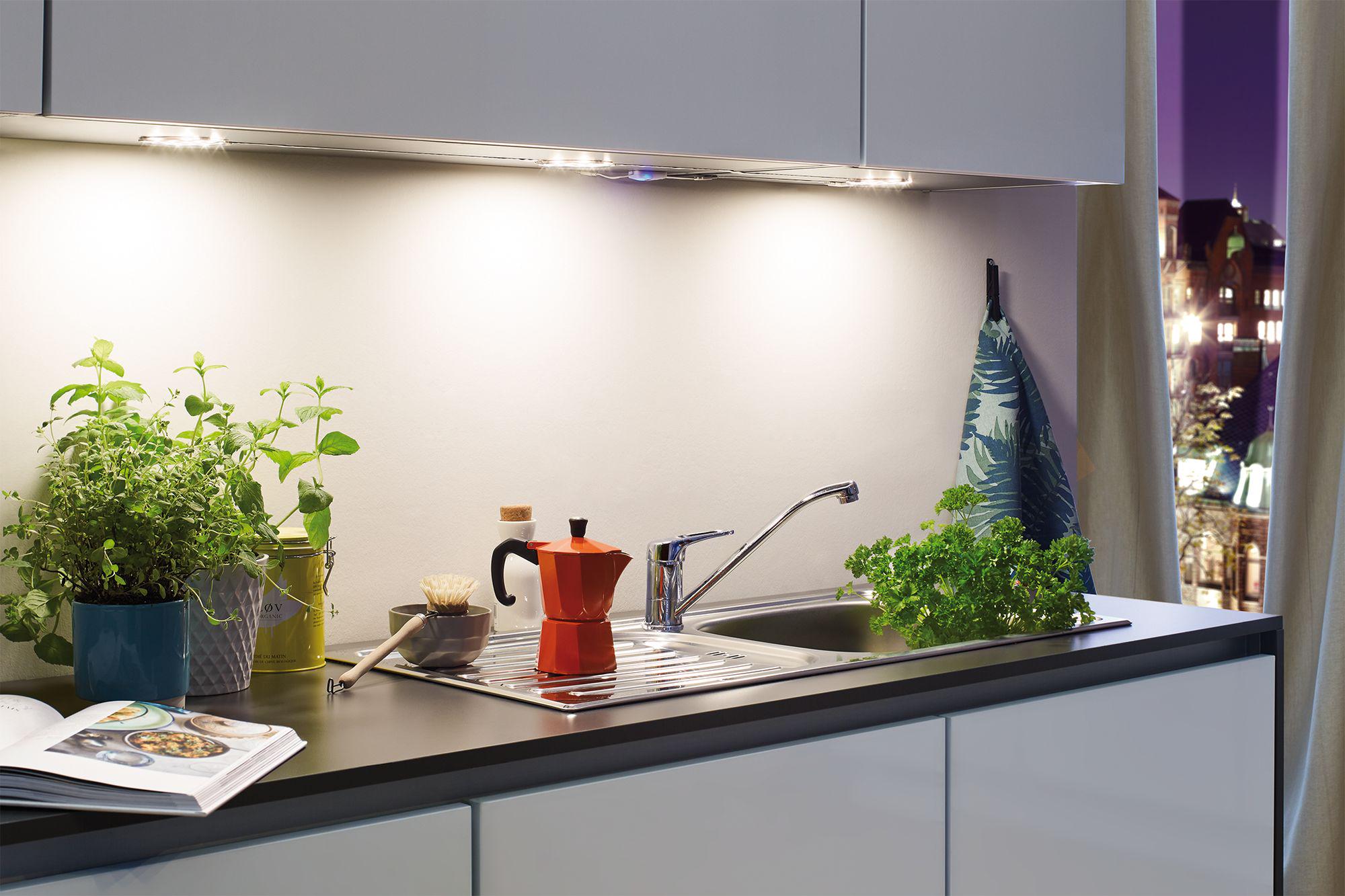 Modern kitchen countertop with stainless steel sink, red espresso maker, and LED under-cabinet lights.