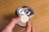 Hand holding round LED light module with metal base on wooden surface, LED replacement part for recessed spotlights