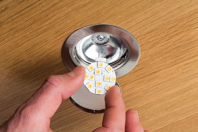 Hand holding round LED light module with metal base on wooden surface, LED replacement part for recessed spotlights