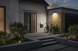 Modern house entrance with grey door, bicycle and outdoor wall light on wooden cladding at dusk