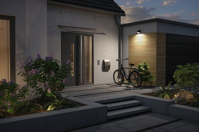 Modern house entrance with grey door, bicycle and outdoor wall light on wooden cladding at dusk