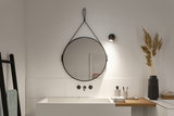 Miroir mural rond noir avec sangle en cuir et applique LED noire au-dessus d'un lavabo blanc