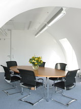 Moderne vergadertafel met houten blad en zes zwarte mesh stoelen in lichte kantoorruimte met LED-plafondlampen