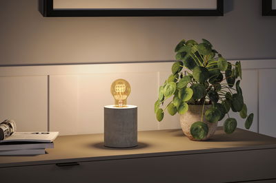 Modern table lamp with concrete cylinder base and warm glowing bulb light on sideboard.