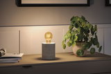 Moderne Tischlampe mit Zylindersockel aus Beton und warmem Glühbirnenlicht auf Sideboard.