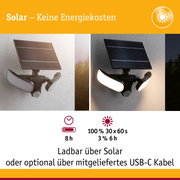 Schwarze Solarleuchte mit drei weißen LED-Lichtflächen an weißer Wand, energiesparende Außenbeleuchtung