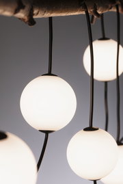 Moderne Pendelleuchte mit weißen Glas-Kugeln und schwarzen Kabeln an Holzdecke für Wohnraumbeleuchtung