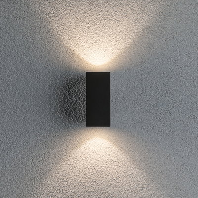 Black aluminum wall light casting warm white light up and down on textured grey wall