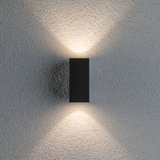 Applique murale noire en aluminium diffusant une lumière blanche chaude vers le haut et le bas sur mur gris texturé