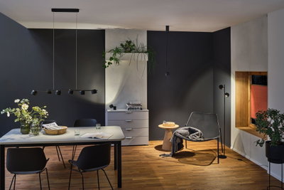 Salon moderne avec suspension et lampadaire noirs en métal, sol en bois et fauteuil gris