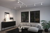 Modern living room with white ceiling track lights, grey corner sofa, and black wooden sideboard for home lighting.