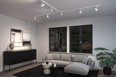 Modern living room with white ceiling track lights, grey corner sofa, and black wooden sideboard for home lighting.