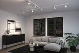 Salon moderne avec éclairage sur rail blanc au plafond, canapé d'angle gris et buffet noir en bois.