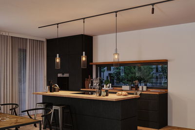 Moderne Küche mit schwarzer Holzinsel und drei schwarzen Metall-Hängelampen mit warmem Licht.