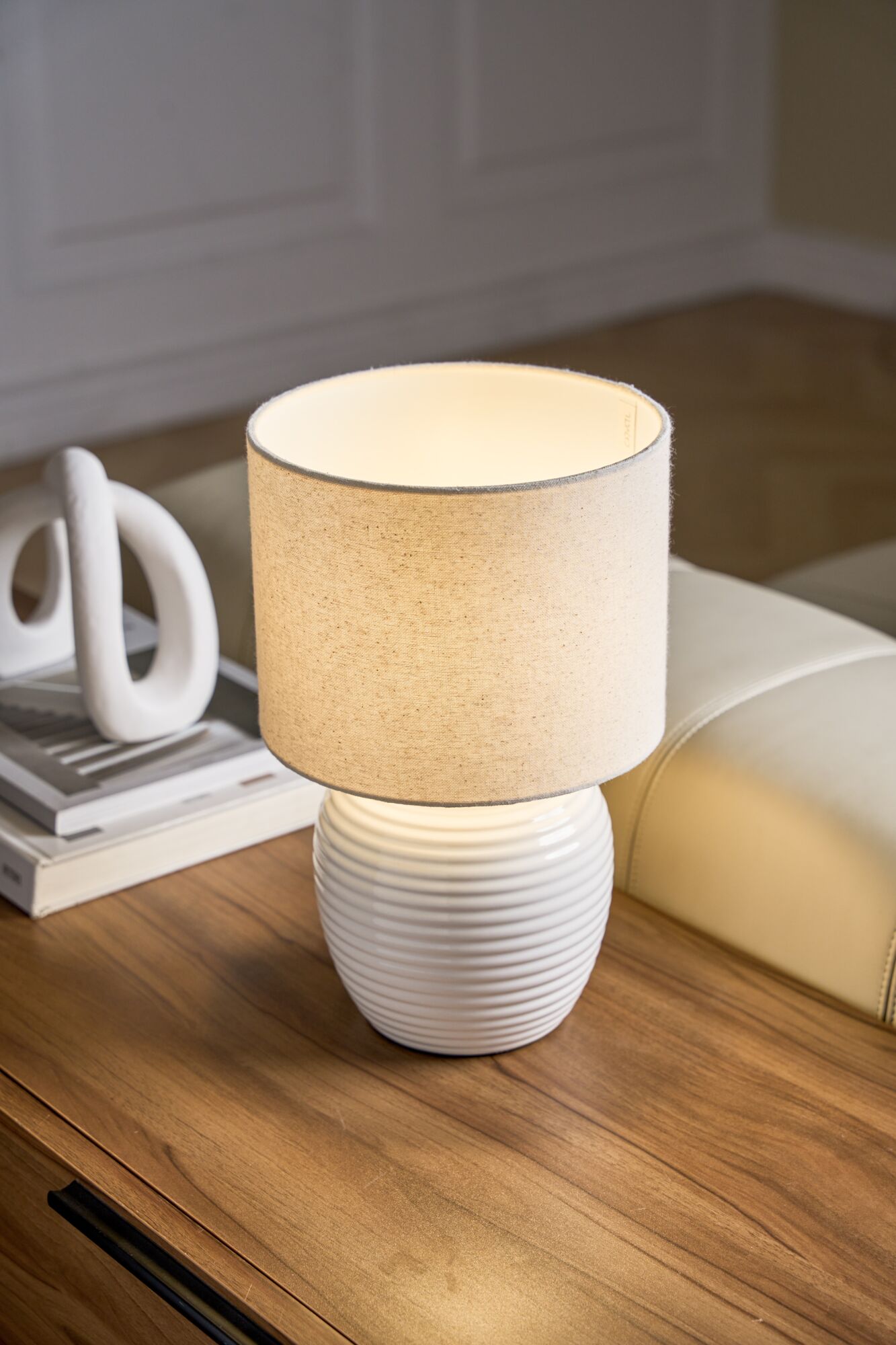 Tafellamp met witte keramische voet en beige stoffen kap op houten tafel voor sfeerverlichting