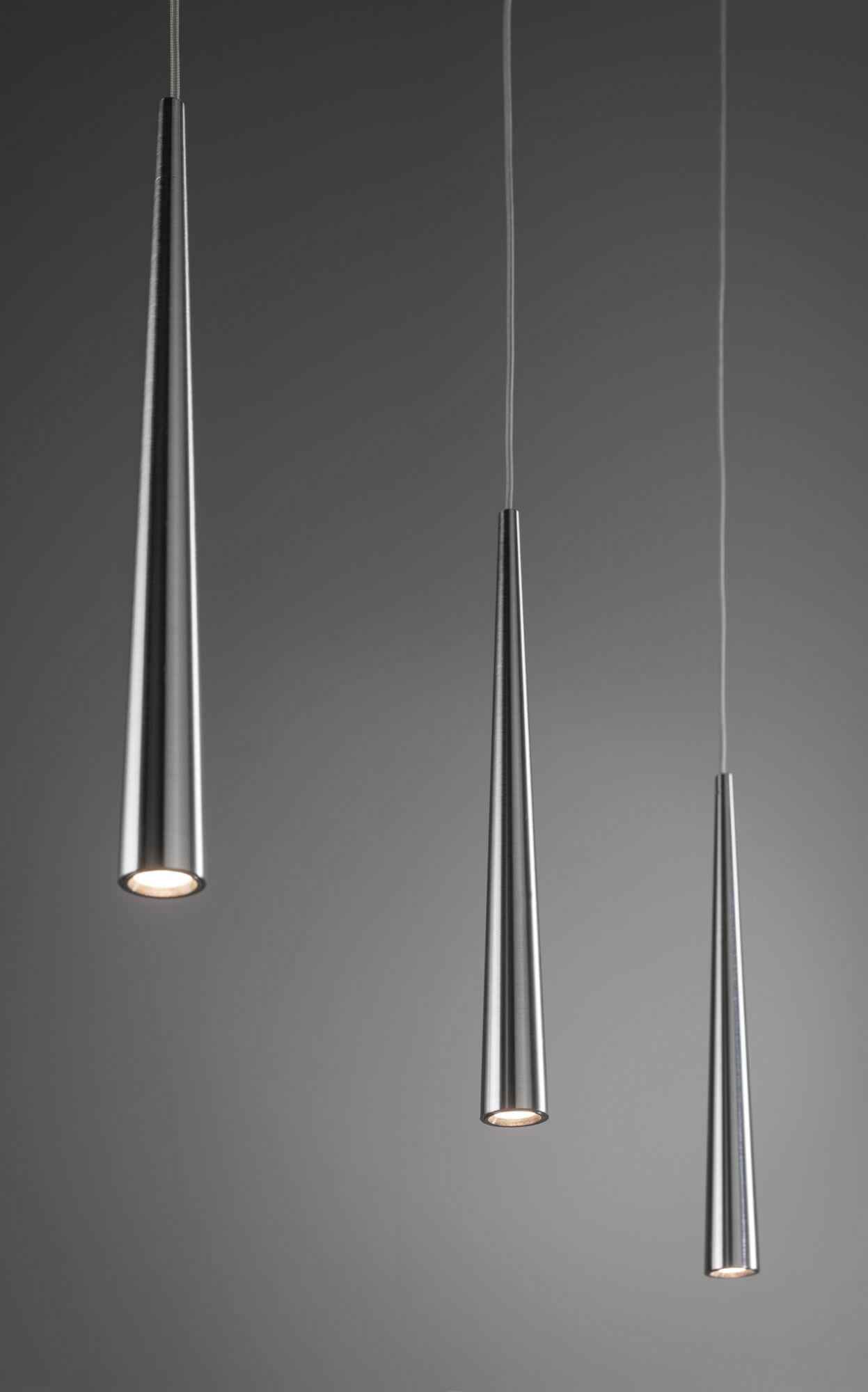 Drei schlanke Pendelleuchten aus gebürstetem Aluminium in Silber mit warmweißem LED-Licht.