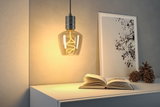 Hanging LED bulb with warm white light and grey metal holder above white sideboard with book and decor.