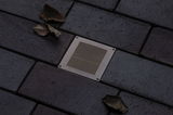 Recessed square stainless steel floor light with grid pattern on dark paving stones with autumn leaves