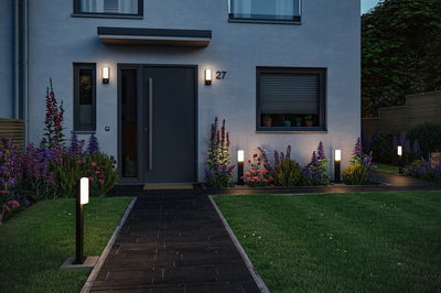 Modern outdoor lighting with black LED post lamps and wall lights on house facade and garden path.