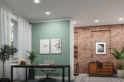 Modernes Büro mit grün gestrichener Wand, schwarzem Tisch und Stuhl, Akzentwand aus rotem Backstein und Holzkommode