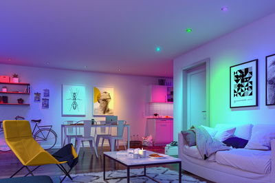 Modernes Wohnzimmer mit farbigen LED-Einbaustrahlern in Weiß, Gelb und Grün, gemütliche Einrichtung mit Sofa und Stuhl