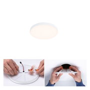 Round white plastic LED ceiling light with warm white glow, hands demonstrating installation steps