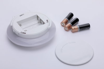 Compartiment rond blanc pour piles avec couvercle et trois piles AA sur fond blanc, accessoire LED