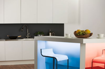 Moderne witte keukenbar met blauwe en rode LED-verlichting, transparante barkrukken en houten fruitschaal