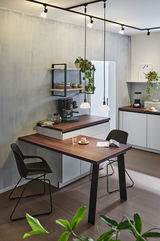 Cuisine moderne avec plan de travail en bois, chaises noires et éclairage suspendu minimaliste.