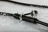 Black waterproof cable connector splashed with water, designed for durable outdoor electrical connections