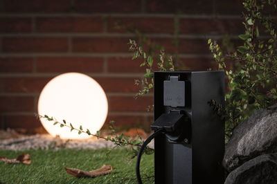 Black outdoor socket with IP44 protection near glowing garden globe light on grass with stones